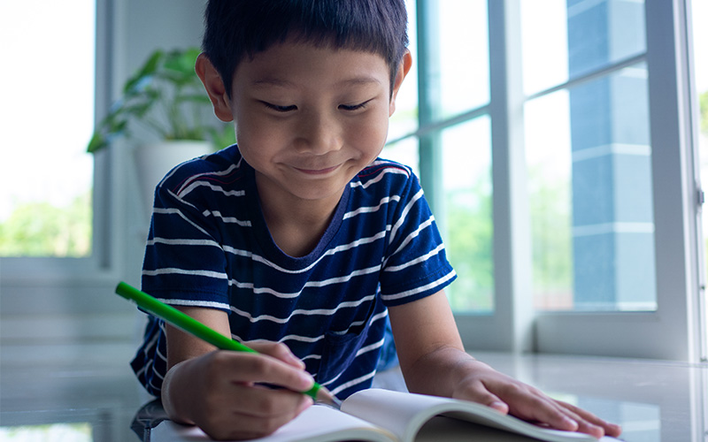 Child writing in notebook near window.